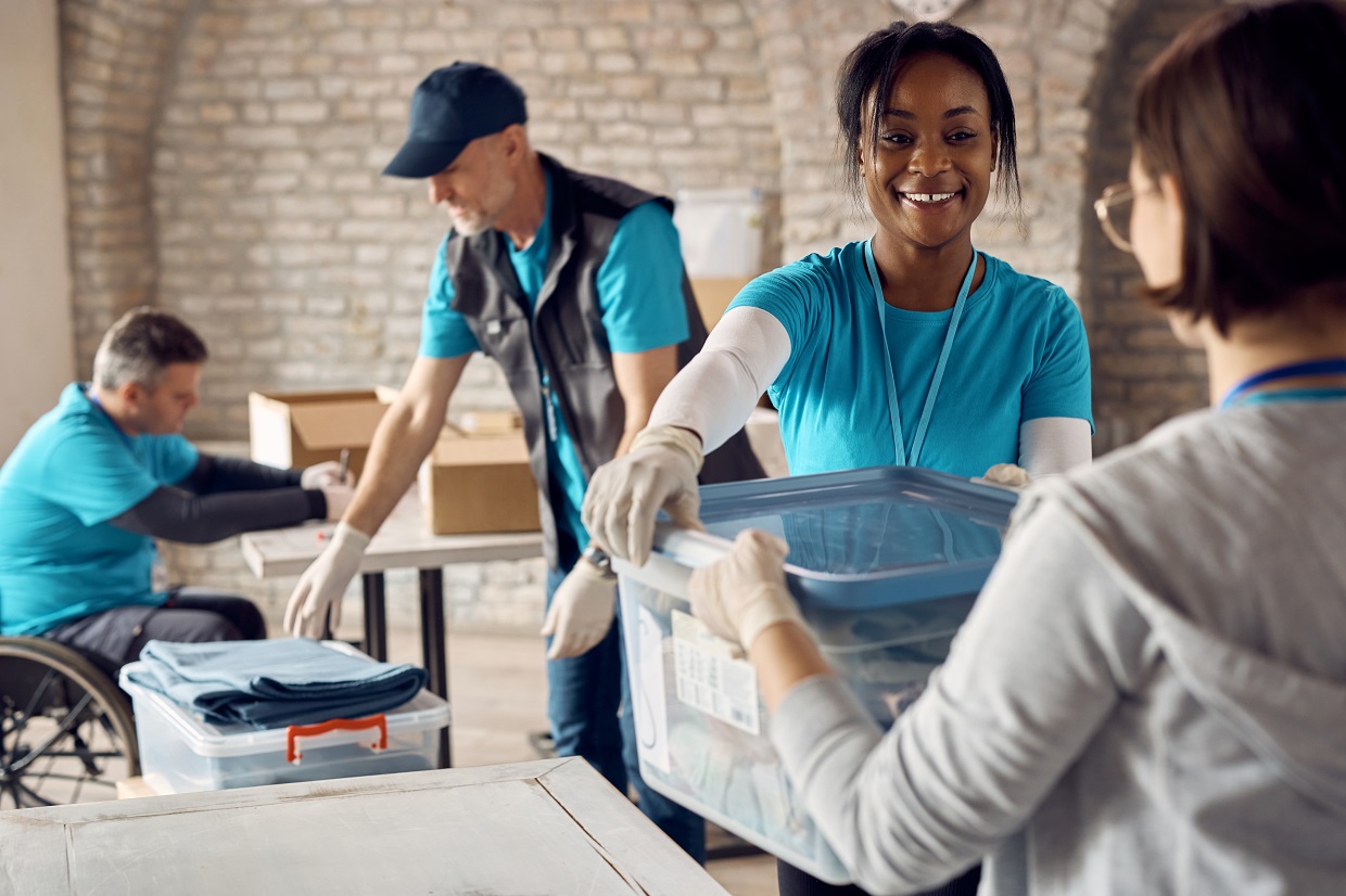 Happy African American volunteer and her coworkers cooperating while preparing donation boxes at charitable foundation.
